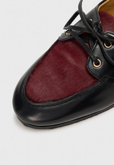 Black leather shoe featuring a maroon, soft-textured panel on the upper, with gold eyelets and matching black laces.