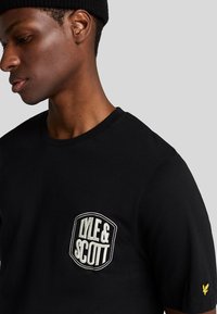 T-shirt in cotone nero con logo Lyle & Scott ricamato bianco sul petto, maniche corte e colletto rotondo.