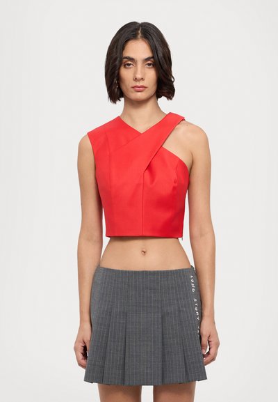 Červený cropped top s asymetrickým designem, který má široký ramínko. Spárovaný s šedou mini sukní s plisováním a vertikálními pruhy.