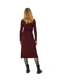 Długa bordowa sukienka z prążkowanego dzianiny z dopasowanym topem i rozkloszowaną spódnicą o długości midi, zestawiona z czarnymi botkami za kostkę. Prosty i teksturowany fason.