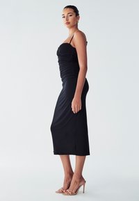 Black midi dress with ruched bodice and thin straps, smooth texture, fitted silhouette, featuring a straight hem and subtle side slit.