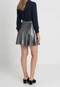 Jupe patineuse argentée métallisée avec une taille ajustée et un design évasé, associée à un blouse noire à manches longues et des chaussures à talons carrés noires.