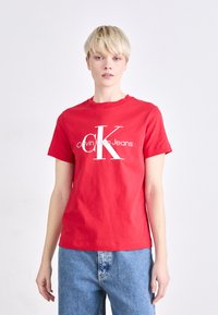 Rode katoenen T-shirt met korte mouwen, voorzien van een wit "Calvin Klein Jeans" logo en een groot "CK" grafisch ontwerp op de voorkant. Casual fit.
