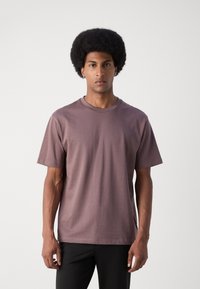 Tricou cu mânecă scurtă și guler rotund, din bumbac moale de culoare mauve estompată, având un croi lejer și o textură uniformă.