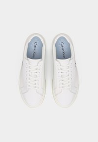 Ζευγάρι λευκά δερμάτινα παπούτσια Calvin Klein με λευκά κορδόνια, ορατό λογότυπο της μάρκας στο εσωτερικό, παρουσιασμένα από πάνω σε λευκό φόντο.