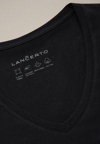 Czarna koszulka z dekoltem w kształcie litery V wykonana z elastycznej, oddychającej bawełny. Charakteryzuje się gładką teksturą oraz czytelnymi nadrukowanymi metkami z informacjami o pielęgnacji i właściwościach materiału.