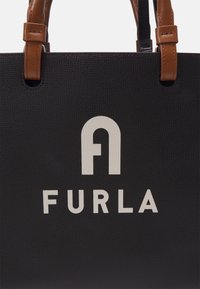 Czarna torebka o teksturowanej powierzchni z brązowymi skórzanymi uchwytami oraz białym logo i herbem "FURLA" na środku przodu.