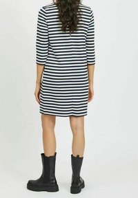 Námořnické a bílé pruhované šaty se třičtvrtinovými rukávy, délka nad kolena, v kombinaci s černými kotníkovými botami. Hladká textilie.