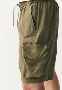Shorts verts olive en tissu léger, avec une taille élastique, des poches latérales et une grande poche cargo sur la cuisse.