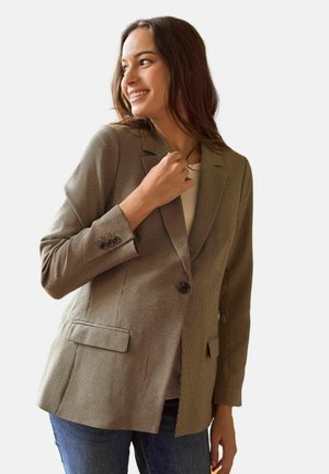Brun ternet blazer med hakkede revers, to forlommer og knaplukning. Båret over en lys top, kombineret med blå jeans.