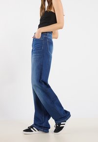 Breda ben blå jeans i denim med ljus tvätt, med framfickor och standardstickning, kombinerat med svarta sneakers.