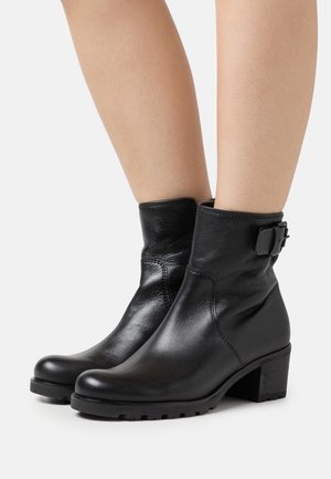 Bottines en cuir noir avec une texture lisse, dotées d'un talon carré, de détails de boucle sur le côté et d'une conception à bout rond.