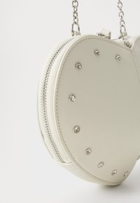 White round purse made of faux leather. Features a silver zipper and decorative rhinestones on the surface. Chain strap included.