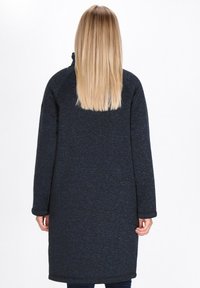 Cappotto lungo di un blu scuro, realizzato in un tessuto a maglia testurizzato. Presenta un colletto alto e maniche lunghe, arriva fino a metà coscia, con una vestibilità rilassata.
