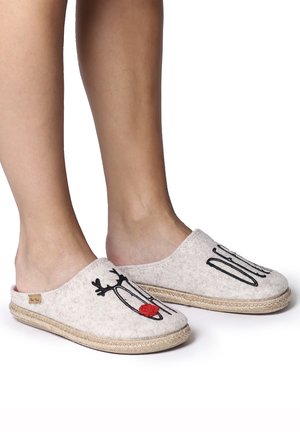 Fødder iført beige slip-on tøfler med broderet rensdyransigt og rød næse, stående på en hvid overflade.