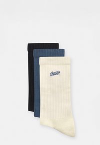 Trei perechi de șosete ribbed: negre, bleumarin și crem. Fiecare pereche are un tiv confortabil și un mic logo brodat pe perechea crem.