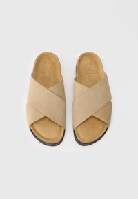 Sandali incrociati in suede beige con una morbida soletta, punta aperta e suola testurizzata. Presentano dettagli cuciti e un design minimalista.