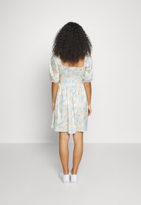 Vestido floral com mangas bufantes e costas quadradas, nas cores azul pastel, amarelo e rosa. Usado com sapatilhas brancas.