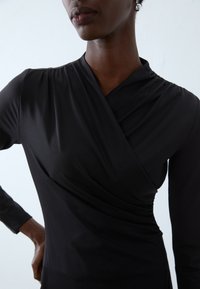 Black long-sleeve top with a wrap-style design, featuring soft, smooth fabric and gathered detailing at the shoulders and waist.