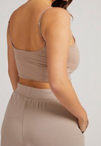 Jasnobrązowy krótki top z regulowanymi ramiączkami, gładką fakturą i dopasowanym krojem, w połączeniu z dopasowanymi spodniami z wysokim stanem.