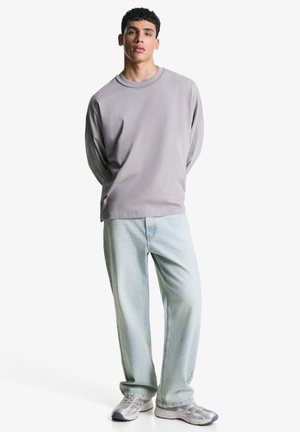 Lichtgrijze longsleeve met een ronde hals, gecombineerd met losse lichtblauwe denim jeans en grijze sneakers. Eenvoudig ontwerp, minimale accenten.