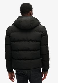 Czarna kurtka puchowa z kapturem, z pikowanym wzorem, elastycznymi mankietami i detalem logo na plecach. Wykonana z gładkiego, wodoodpornego materiału.