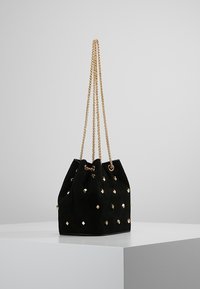 Borsa a secchiello in suede nero con manici in catena dorata, caratterizzata da piccoli chiodini quadrati dorati distribuiti uniformemente sulla superficie.