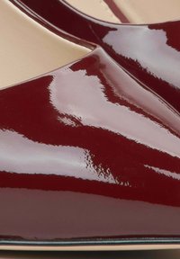 Bordeaux patenten leren pumps met een glanzende afwerking, voorzien van een puntige neus en een minimalistisch ontwerp, dat de soepele textuur en slanke vorm benadrukt.
