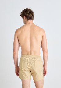 Shorts de bain beiges avec une taille élastique et une poche arrière, vus de l'arrière. Texture lisse et design simple.