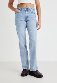 Lichtblauwe denim jeans met een hoge taille, rechte pijpen, subtiele vervaging en een klassieke five-pocket indeling, gecombineerd met zwarte schoenen.