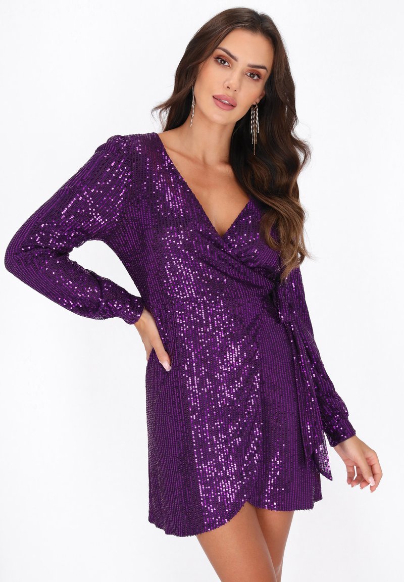 Violet sequin-mekko, jossa on pitkät hihat, V-pääntie ja kietaisumalli. Täynnä kimaltelevaa pintaa ja lyhyt helma.