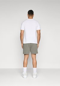 T-shirt branca de manga curta combinada com calções verde-azeitona. O modelo utiliza meias brancas e sapatilhas brancas desportivas. Um conjunto simples e casual.