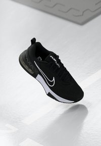 Svarta Nike Air Max löparskor med vit swoosh och sula, visade i luften över en reflexiv vit yta.