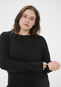 Haut noir à manches longues avec un col rond, fabriqué en tissu doux. Présente des manches ajustées avec des trous pour les pouces pour un confort accru.