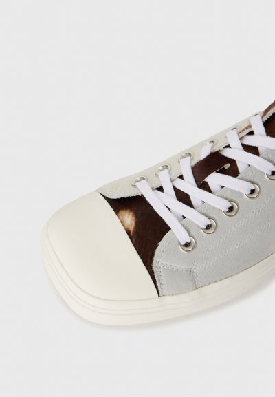 Ljusgrå sneakers med en brun- och vitmönstrad panel, gummitåhatt och vita skosnören. Mjuk textur med metallögglor för snörena.