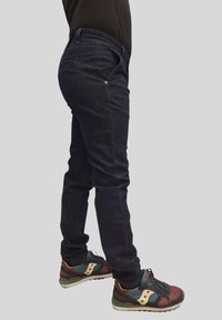 Pantaloni slim-fit blu scuro, caratterizzati da un design elegante e da dettagli di cucitura discreti, abbinati a scarpe sportive multicolori.