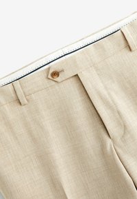 Hellbeige Leinenhosen mit glatter Textur, ausgestattet mit einem Knopfverschluss und einem kontrastierenden marineblauen Innenfutter im Bund.
