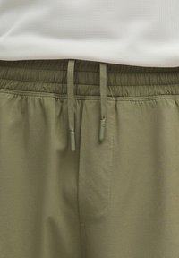 Pantalones cortos deportivos verde oliva hechos de una tela suave, con una cintura elástica con cordones ajustables y bolsillos laterales.