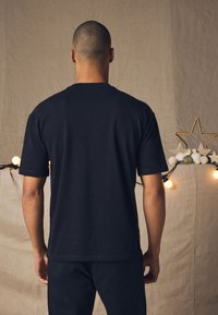 Black cotton t-shirt with a crew neckline, short sleeves, and a relaxed fit, shown from the back against a neutral backdrop.