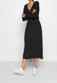 Robe noire midi à manches longues, décolleté en V et détail à nouer. Stylisée avec des baskets blanches, dotée d'un design fluide et d'une taille élastique.