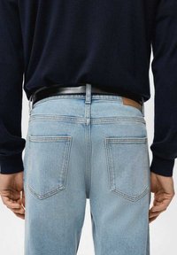 Vaqueros de mezclilla azul claro con corte recto, dos bolsillos traseros y detalles cosidos. Combinados con un cinturón negro y una camiseta azul marino.