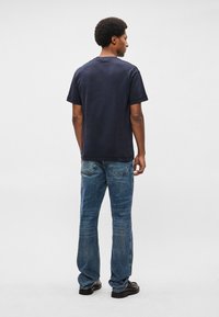 Μαρίνα βαμβακερή μπλούζα με χαλαρή εφαρμογή, κοντά μανίκια και λαιμόκοψη, συνδυασμένη με ξεθωριασμένο μπλε τζιν παντελόνι που διαθέτει δύο πίσω τσέπες.