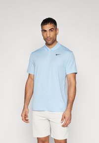 T-shirt polo azul claro feito de tecido suave, com um logo preto da Nike no lado esquerdo do peito, mangas curtas e um design de colarinho clássico.