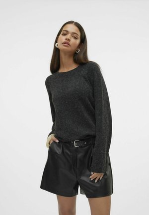Donkergrijze gebreide trui met lange mouwen, gecombineerd met hoge zwarte leren shorts. Opmerkelijke ronde witte oorbellen worden gedragen.