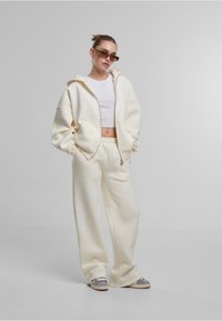 Haut à capuche oversized couleur crème et pantalon de survêtement assorti, fabriqués en tissu doux. Comprend une fermeture éclair et une taille ajustable avec cordon.