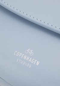 Světlá modrá kožená taška s hladkou texturou, zdobená bílým prošitím a vyraženým logem "COPENHAGEN STUDIOS" s ikonou kola.