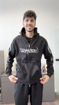 Svart zip hoodie med en stor grafisk logotyp på framsidan och detaljerade mönster på ärmarna. Har en avslappnad passform och en huva.