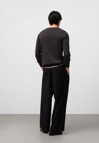 Dunkelgrauer, langärmeliger Strickpullover, kombiniert mit lockeren, schwarzen Hosen. Die Hosen haben seitliche Taschen, und die Schuhe sind schwarz.