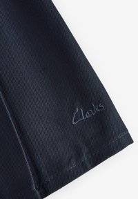 Scarpa in tessuto blu navy con design testurizzato e logo "Clarks" ricamato in blu. Presenta un taglio pulito e una finitura senza cuciture.