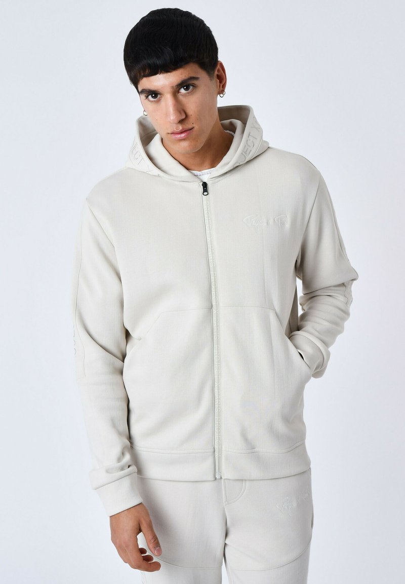 Hoodie zippé beige clair avec une capuche à cordon, poches avant et accents de logo. Tissu à texture douce, bords-côtes aux poignets et à l'ourlet.